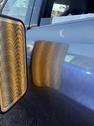 Reflection board revealing a dent's contour on a car door panel during paintless dent repair